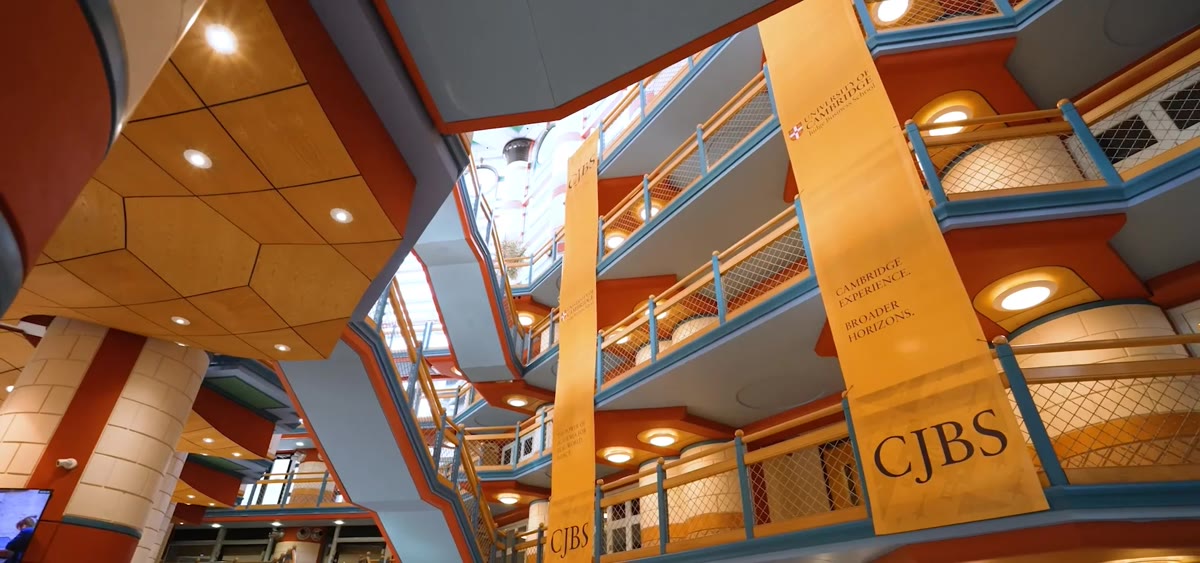 The atrium of a Cambridge business school, seen from the ground floor: galleried balconies rising four storeys under a skylight.